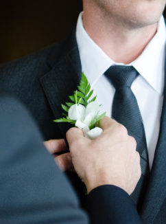 A friend helps the groom to attach his button hole ready for his wedding day at mercure gloucester bowden hall hotel