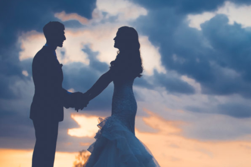 Bride and groom hold hands with dusk sky in background