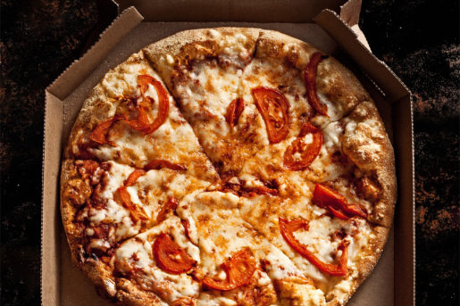 Take-away sliced cheese and tomato pizza in a cardboard box.